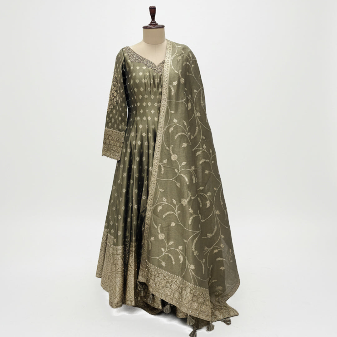 This stunning Anarkali suit comes in a beautiful olive green shade with golden embroidery that gives it a rich and classy look. The long, flowy kurta has a soft shine and delicate patterns all over adding a touch of grace and tradition.

The matching dupatta features fine floral embroidery and a detailed border that perfectly compliments the outfit.

Simple yet sophisticated, this set is ideal for festive gatherings, weddings or formal events where you want to look graceful and timeless.