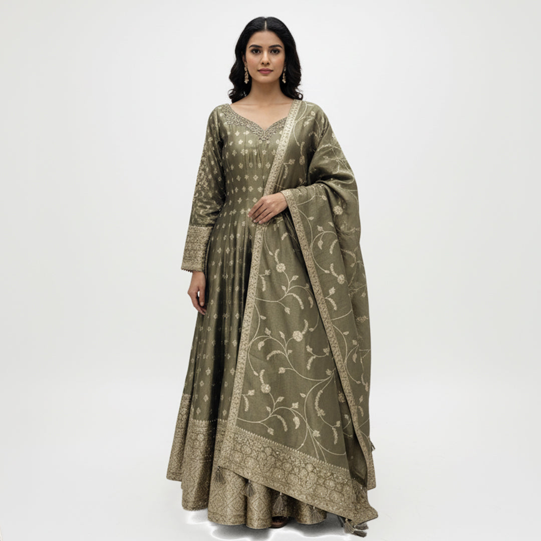 This stunning Anarkali suit comes in a beautiful olive green shade with golden embroidery that gives it a rich and classy look. The long, flowy kurta has a soft shine and delicate patterns all over adding a touch of grace and tradition.

The matching dupatta features fine floral embroidery and a detailed border that perfectly compliments the outfit.

Simple yet sophisticated, this set is ideal for festive gatherings, weddings or formal events where you want to look graceful and timeless.