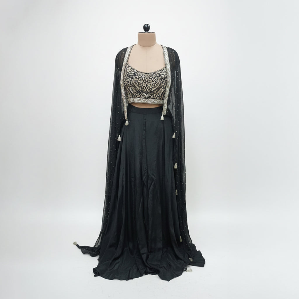 Modernize your ethnic style with this 3-piece Midnight Black Indo-Western Set. It features a hand-embroidered mirror-work bustier paired with a flowing silk skirt and a sheer, sequin-sprinkled georgette cape. This sleek, monochromatic look offers a sophisticated alternative to traditional wear, making it an ideal pick for cocktail nights and high-end receptions.