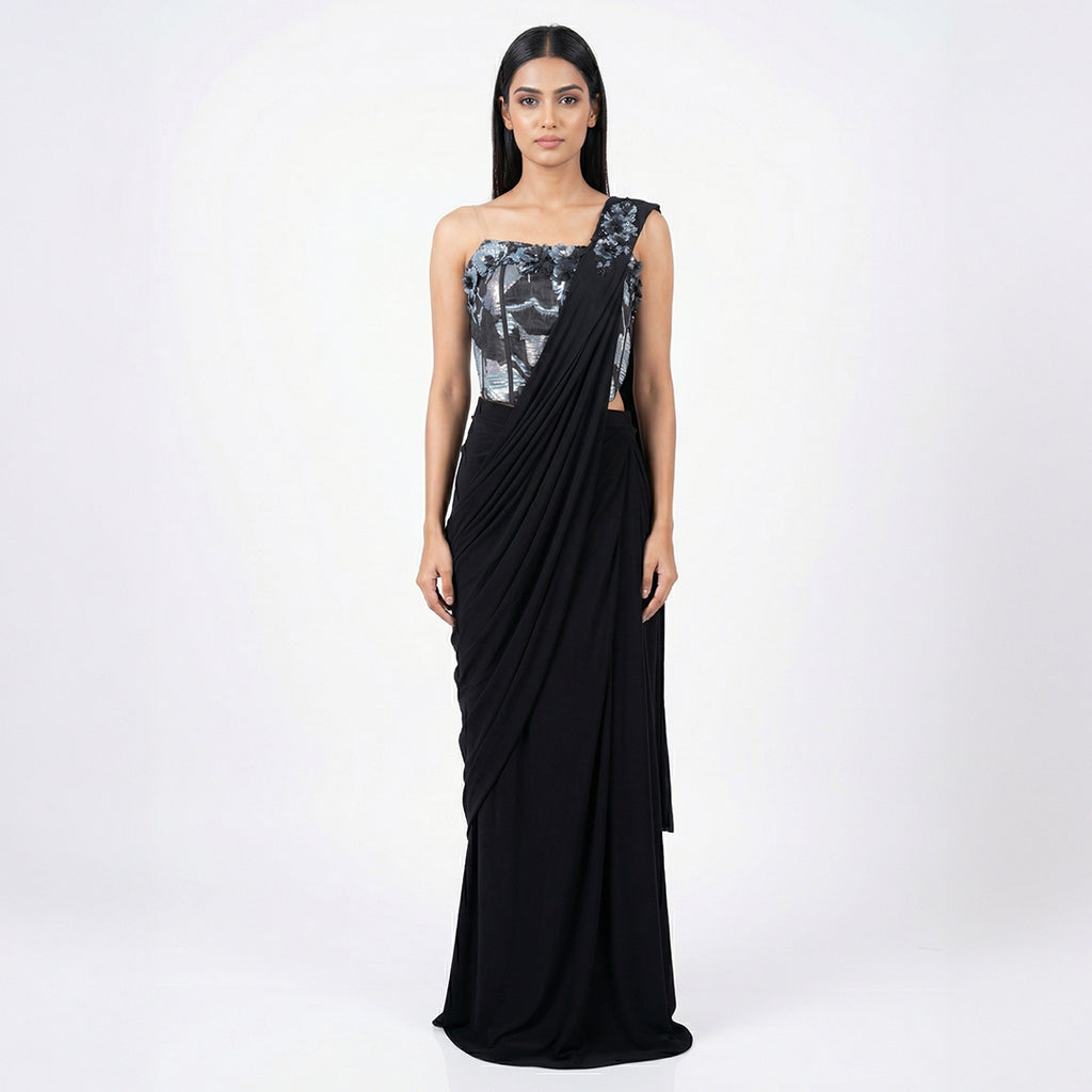 This is a stylish outfit is in a stunning black color. It features a trendy corset-style blouse with shiny silver patterns and beautiful flower designs on the shoulder.

It comes with a pre-draped saree that is very easy to wear and flows perfectly. This outfit is modern, fancy, and perfect for cocktail parties, receptions, and evening events.