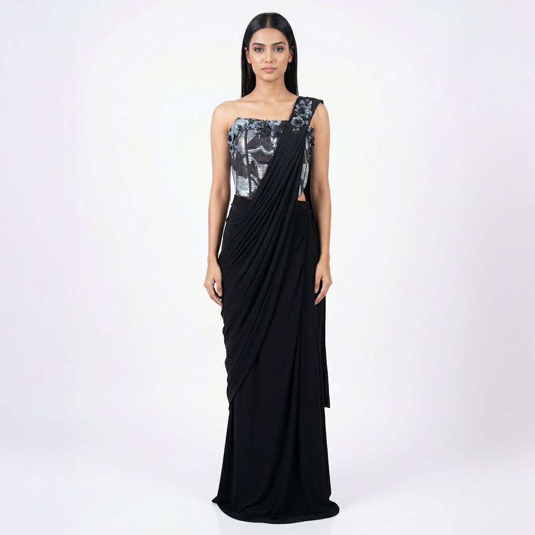 This is a stylish outfit is in a stunning black color. It features a trendy corset-style blouse with shiny silver patterns and beautiful flower designs on the shoulder.

It comes with a pre-draped saree that is very easy to wear and flows perfectly. This outfit is modern, fancy, and perfect for cocktail parties, receptions, and evening events.