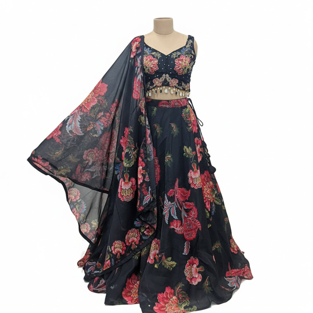 This beautiful lehenga is in a classic black color. The blouse features colorful flower embroidery and has cute beaded hangings at the bottom.

The skirt and matching dupatta have a big, bright floral print with red and pink flowers that look very fresh.

This outfit is elegant, vibrant, and perfect for sangeet nights, weddings, and festive parties.
