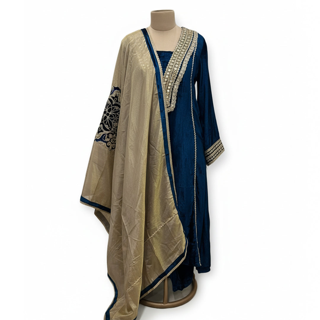 This rich outfit is perfect for the winter season. It is made from soft and warm velvet fabric in a lovely deep teal blue color.

The long kurta has beautiful shiny mirror work and golden patterns on the neckline and sleeves to give it a festive look.

It comes with a contrasting golden dupatta that drapes nicely. This outfit is cozy, elegant, and great for winter weddings and parties.