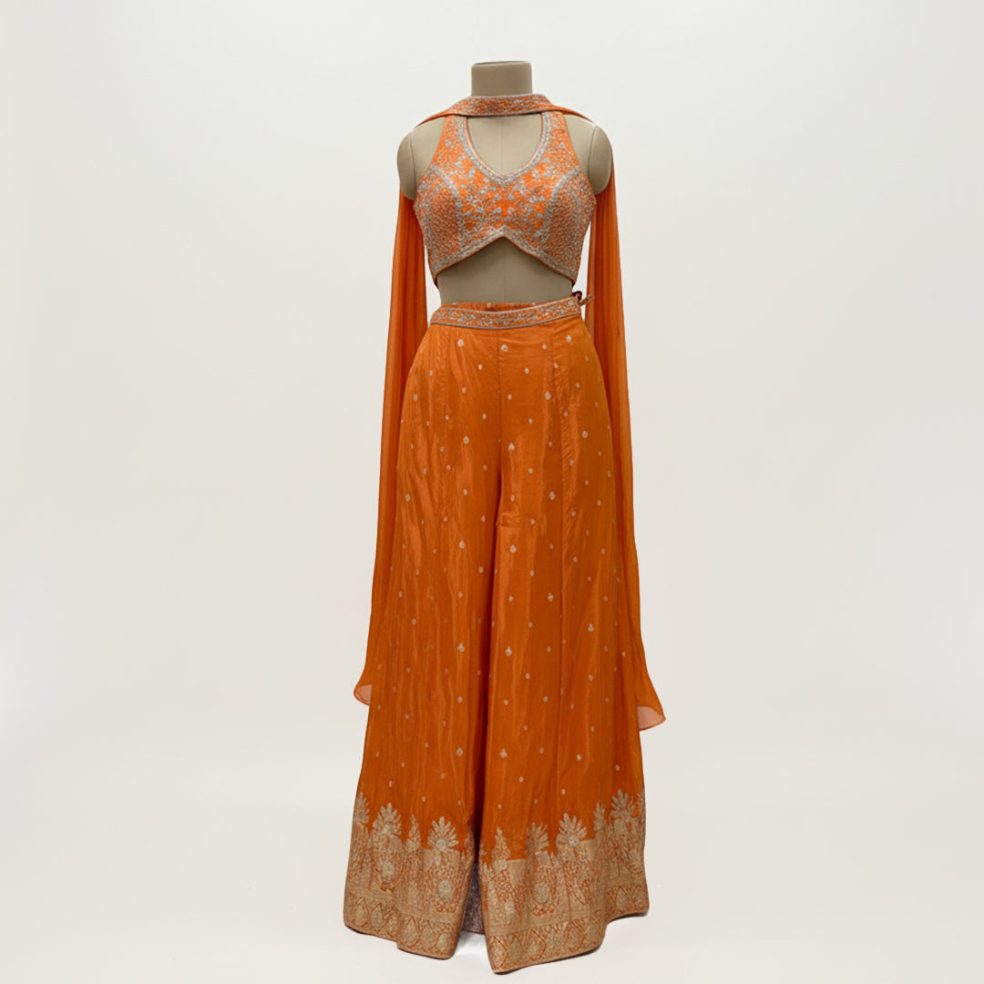 This is a bright orange outfit with a stylish embroidered blouse and palazzo. The blouse has a modern cut with silver detailing that adds sparkle and charm.

The palazzo is flowy with delicate embroidery and a detailed border at the hem.

The matching dupatta drapes lightly, completing the elegant look.
Perfect for mehndi, haldi or festive celebrations. It’s trendy, vibrant and full of festive flair.