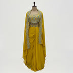 This is a bright yellow Indo-western outfit featuring a heavily embellished blouse paired with a matching skirt and a cape.&nbsp;

The blouse is beautifully decorated with silver and turquoise embroidery, adding sparkle and elegance.

The flowy skirt drapes softly, while the cape, edged with detailed embroidery, adds a stylish and graceful touch. Perfect for weddings, haldi, mehandi receptions or festive occasions.&nbsp;