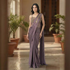 This stylish outfit is a pre-draped saree in a beautiful deep mauve color. It features a trendy corset-style blouse with thin straps and intricate gold embroidery on the upper part. The saree is draped perfectly with neat pleats in the front, and the fabric feels smooth and silky. The look is completed with an embroidered border on the shoulder drape, making it a modern and elegant choice for cocktail parties.