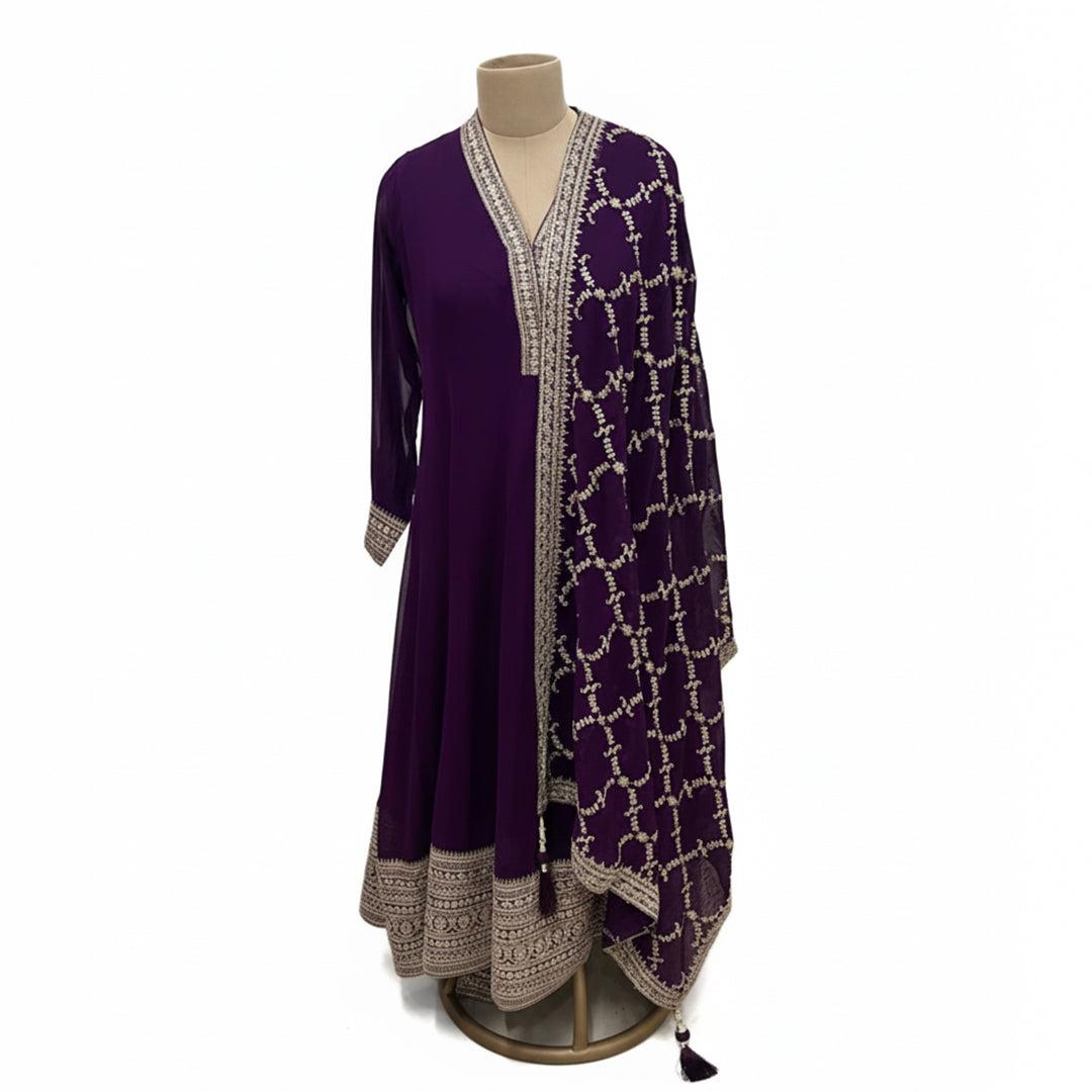 This royal outfit is in a beautiful deep purple color. It features a long, flowy Anarkali kurta with shiny silver embroidery on the neckline, sleeves, and a thick border at the bottom. It comes with comfortable matching palazzo pants. The look is completed with a heavy dupatta that is fully covered in a lovely silver net pattern. This outfit is traditional, elegant, and perfect for weddings and festivals.