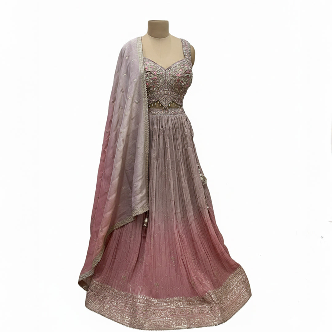 This pretty lehenga comes in soft shades of mauve and pink. The blouse is heavily decorated with silver and pink embroidery for a rich look.

The skirt has a unique crushed texture and a lovely color that fades from light purple to pink at the bottom.

It includes a matching dupatta with small sparkles. This outfit is elegant, dreamy, and perfect for engagement parties and day weddings.