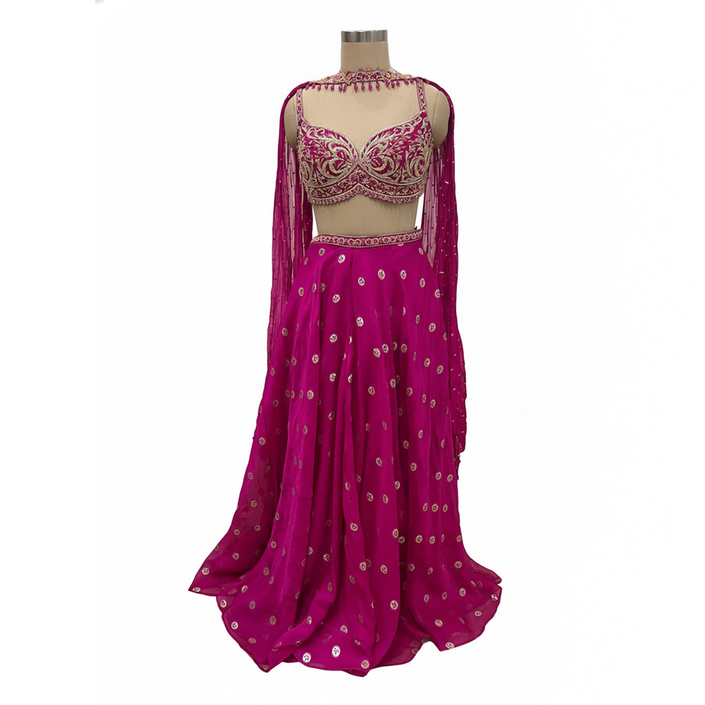 This is a stunning three-piece lehenga choli ensemble in a rich pink color, suitable for festive and formal occasions.

The outfit includes a fitted crop blouse (choli) and a voluminous flared skirt (lehenga) that are heavily embellished with intricate silver-toned embroidery and sparkling accents.

It is completed by a matching sheer overlay scarf (dupatta), featuring latkan around the neck. The ensemble presents a traditional, elegant look.