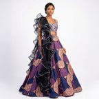 This stylish lehenga outfit features a bold mix of purple, peach, and blue colors. The blouse has shiny embroidery and detailed beadwork for a sparkly look.

It comes with a printed skirt that has a modern, geometric design. The outfit is completed with a unique black dupatta that has big, dramatic ruffles. This outfit is trendy, eye-catching, and perfect for sangeet nights, cocktail parties, and receptions.