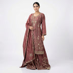 This gorgeous outfit is in a deep wine color. It features a long-sleeved Kurta with beautiful vertical lines of silver embroidery running down the front and floral designs. It is paired with matching wide palazzo pants that are heavily decorated with detailed embroidery at the bottom. The look is completed with a matching dupatta that also features elegant embroidered lines, making it a rich and festive choice
