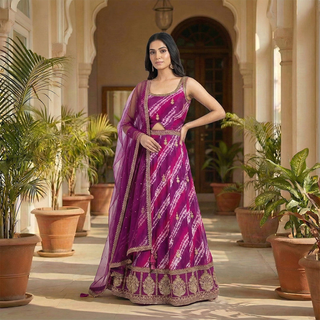 A bright magenta outfit with a beautiful tie-dye pattern and golden embroidery. The top has delicate gold detailing, a scoop neckline, and a small cutout at the waist for a stylish touch. It comes with a matching palazzo that has the same rich color, giving the whole look a perfect festive vibe. The dupatta is light, sheer, and finished with golden borders.