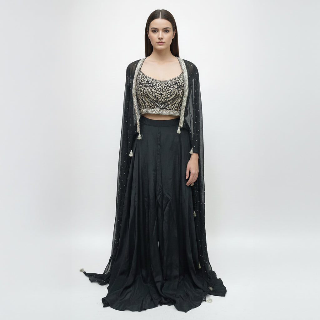 Modernize your ethnic style with this 3-piece Midnight Black Indo-Western Set. It features a hand-embroidered mirror-work bustier paired with a flowing silk skirt and a sheer, sequin-sprinkled georgette cape. This sleek, monochromatic look offers a sophisticated alternative to traditional wear, making it an ideal pick for cocktail nights and high-end receptions.
