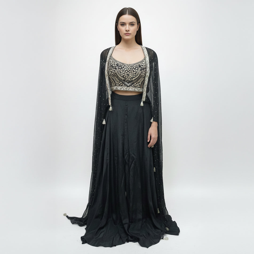 Modernize your ethnic style with this 3-piece Midnight Black Indo-Western Set. It features a hand-embroidered mirror-work bustier paired with a flowing silk skirt and a sheer, sequin-sprinkled georgette cape. This sleek, monochromatic look offers a sophisticated alternative to traditional wear, making it an ideal pick for cocktail nights and high-end receptions.