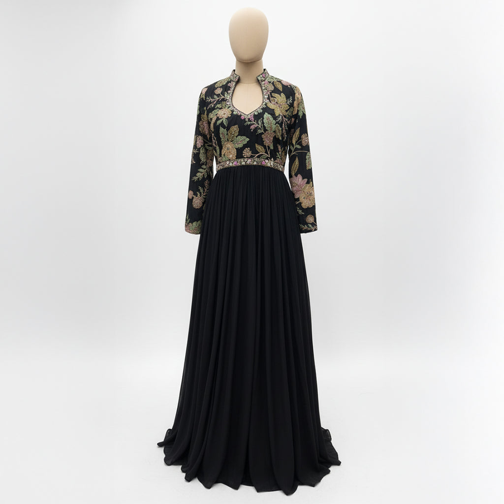 This elegant, full-length black gown features a high-neck bodice adorned with intricate, multi-colored floral embroidery.

The dress has long sleeves and a defined waistline, flowing into a voluminous, pleated skirt that reaches the floor.

The style blends traditional motifs with a modern look, making it a sophisticated choice for formal events or evening wear.