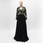 This elegant, full-length black gown features a high-neck bodice adorned with intricate, multi-colored floral embroidery.

The dress has long sleeves and a defined waistline, flowing into a voluminous, pleated skirt that reaches the floor.

The style blends traditional motifs with a modern look, making it a sophisticated choice for formal events or evening wear.