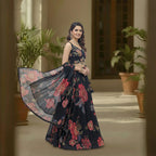 This beautiful lehenga is in a classic black color. The blouse features colorful flower embroidery and has cute beaded hangings at the bottom.

The skirt and matching dupatta have a big, bright floral print with red and pink flowers that look very fresh.

This outfit is elegant, vibrant, and perfect for sangeet nights, weddings, and festive parties.