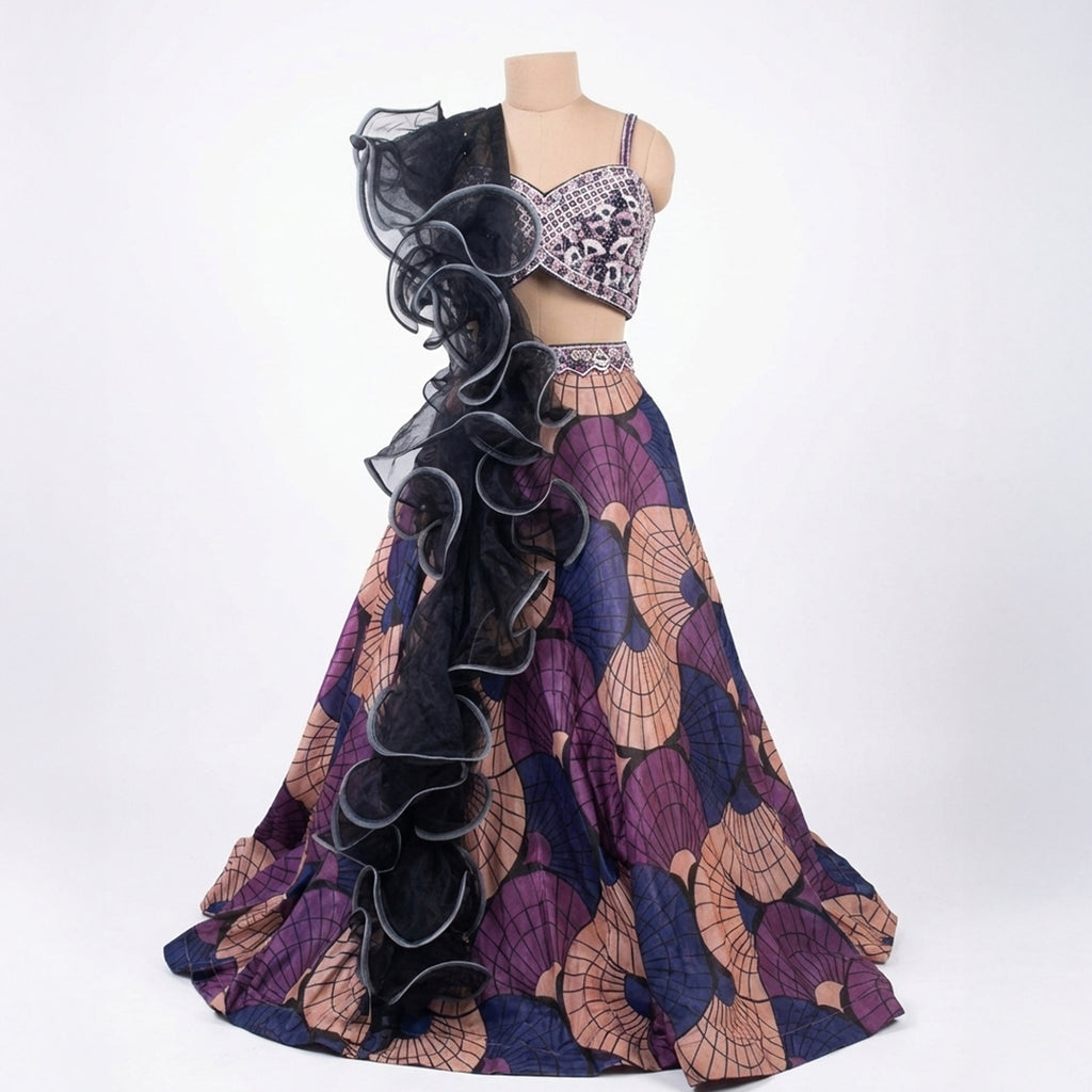 This stylish lehenga outfit features a bold mix of purple, peach, and blue colors. The blouse has shiny embroidery and detailed beadwork for a sparkly look.

It comes with a printed skirt that has a modern, geometric design. The outfit is completed with a unique black dupatta that has big, dramatic ruffles. This outfit is trendy, eye-catching, and perfect for sangeet nights, cocktail parties, and receptions.