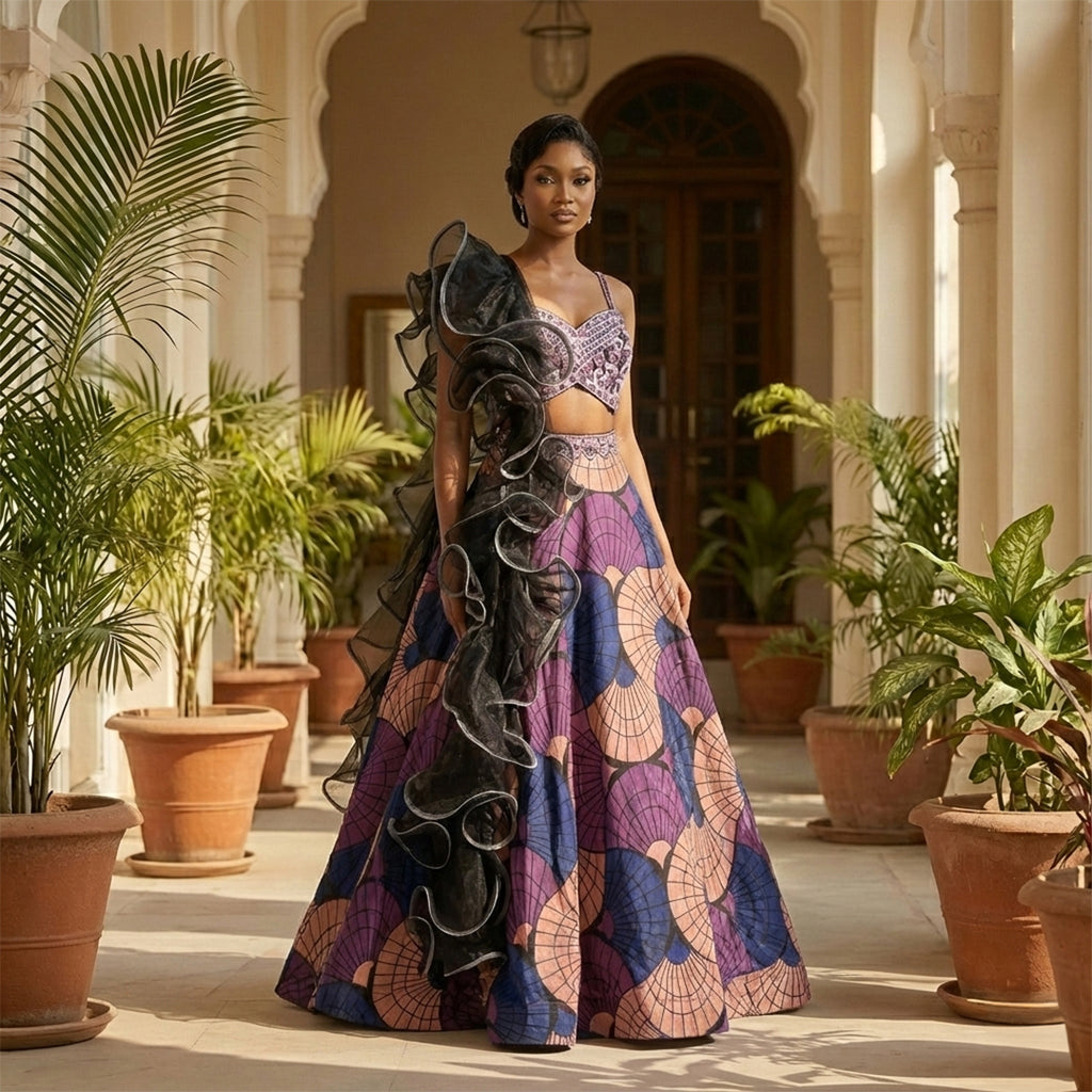 This stylish lehenga outfit features a bold mix of purple, peach, and blue colors. The blouse has shiny embroidery and detailed beadwork for a sparkly look.

It comes with a printed skirt that has a modern, geometric design. The outfit is completed with a unique black dupatta that has big, dramatic ruffles. This outfit is trendy, eye-catching, and perfect for sangeet nights, cocktail parties, and receptions.