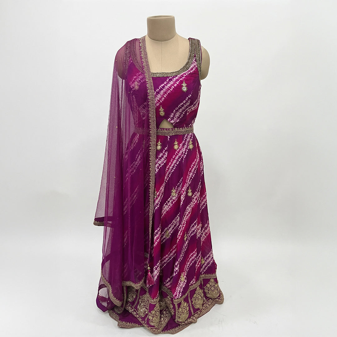 A bright magenta outfit with a beautiful tie-dye pattern and golden embroidery. The top has delicate gold detailing, a scoop neckline, and a small cutout at the waist for a stylish touch. It comes with a matching palazzo that has the same rich color, giving the whole look a perfect festive vibe. The dupatta is light, sheer, and finished with golden borders.