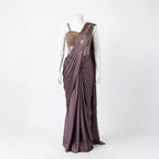 This stylish outfit is a pre-draped saree in a beautiful deep mauve color. It features a trendy corset-style blouse with thin straps and intricate gold embroidery on the upper part. The saree is draped perfectly with neat pleats in the front, and the fabric feels smooth and silky. The look is completed with an embroidered border on the shoulder drape, making it a modern and elegant choice for cocktail parties.