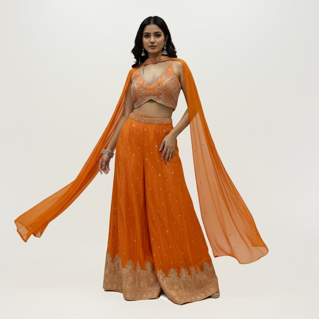 This is a bright orange outfit with a stylish embroidered blouse and palazzo. The blouse has a modern cut with silver detailing that adds sparkle and charm.

The palazzo is flowy with delicate embroidery and a detailed border at the hem.

The matching dupatta drapes lightly, completing the elegant look.
Perfect for mehndi, haldi or festive celebrations. It’s trendy, vibrant and full of festive flair.