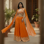 This is a bright orange outfit with a stylish embroidered blouse and palazzo. The blouse has a modern cut with silver detailing that adds sparkle and charm.

The palazzo is flowy with delicate embroidery and a detailed border at the hem.

The matching dupatta drapes lightly, completing the elegant look.
Perfect for mehndi, haldi or festive celebrations. It’s trendy, vibrant and full of festive flair.