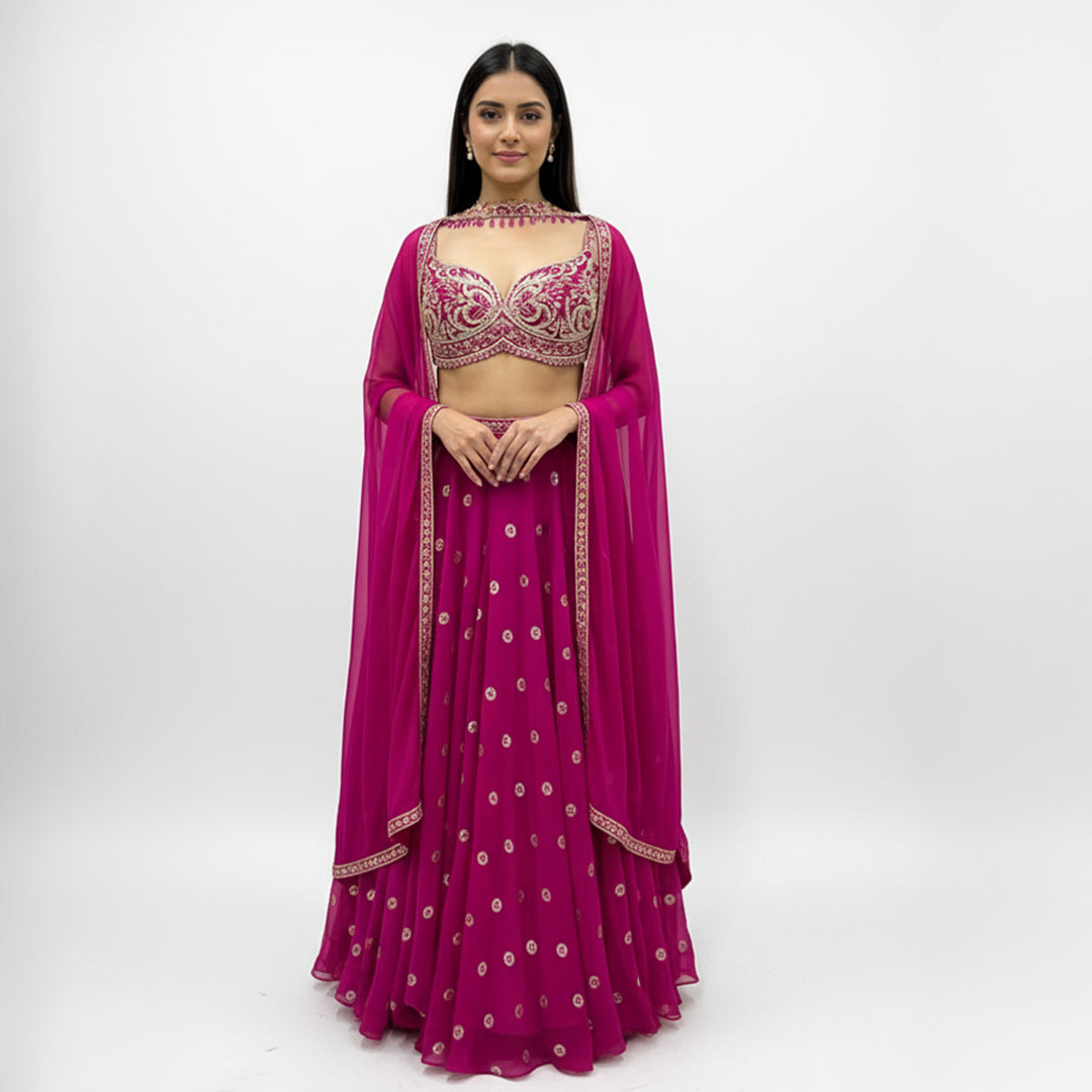 This is a stunning three-piece lehenga choli ensemble in a rich pink color, suitable for festive and formal occasions.

The outfit includes a fitted crop blouse (choli) and a voluminous flared skirt (lehenga) that are heavily embellished with intricate silver-toned embroidery and sparkling accents.

It is completed by a matching sheer overlay scarf (dupatta), featuring latkan around the neck. The ensemble presents a traditional, elegant look.