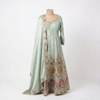 This elegant outfit is in a shiny sea-green color. It features a long, flowy Anarkali kurta with long sleeves and delicate work around the neckline. The bottom of the dress is heavily decorated with colorful red and gold floral embroidery. It comes with matching pants that fit comfortably. The look is finished with a matching Dupatta that has a beautiful embroidered border, making it perfect for weddings and festivals