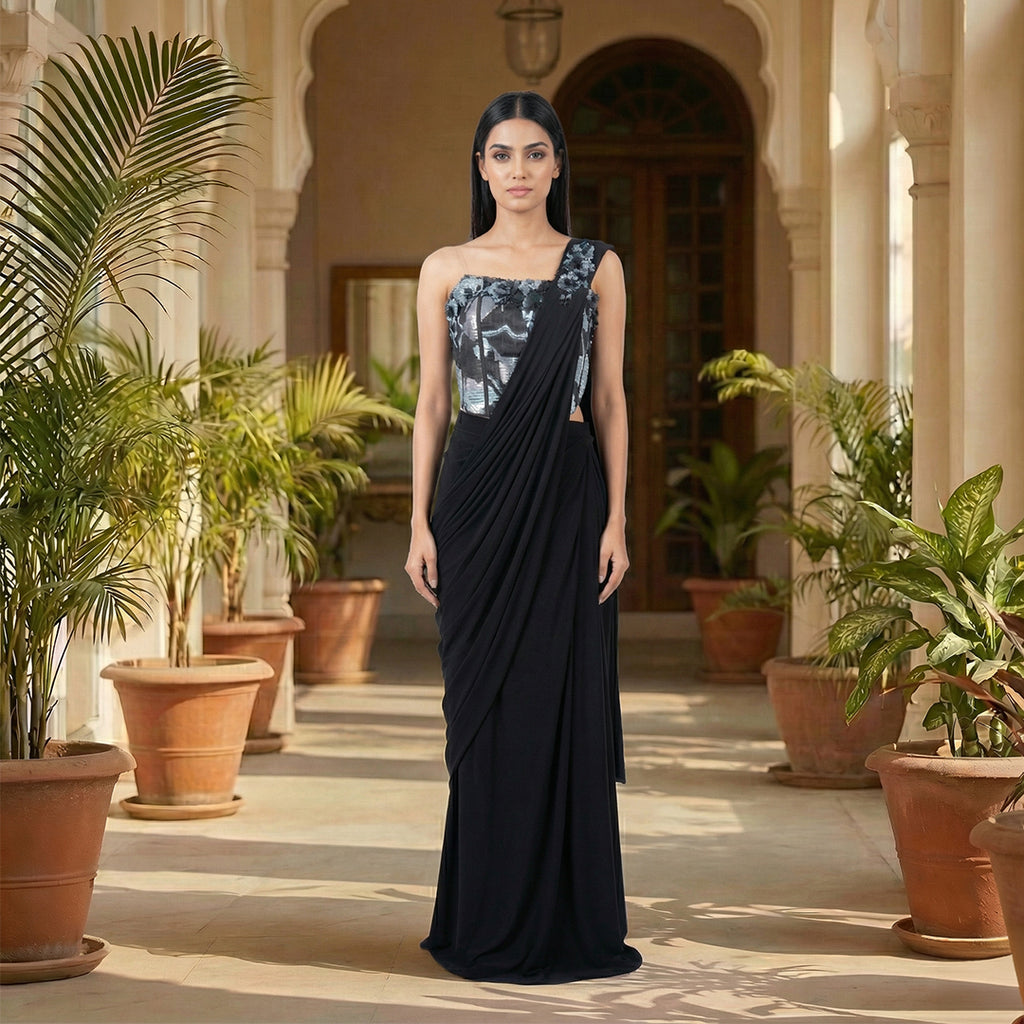 This is a stylish outfit is in a stunning black color. It features a trendy corset-style blouse with shiny silver patterns and beautiful flower designs on the shoulder.

It comes with a pre-draped saree that is very easy to wear and flows perfectly. This outfit is modern, fancy, and perfect for cocktail parties, receptions, and evening events.