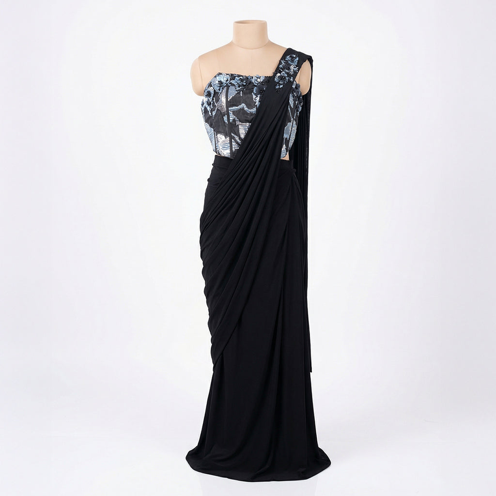 This is a stylish outfit is in a stunning black color. It features a trendy corset-style blouse with shiny silver patterns and beautiful flower designs on the shoulder.

It comes with a pre-draped saree that is very easy to wear and flows perfectly. This outfit is modern, fancy, and perfect for cocktail parties, receptions, and evening events.