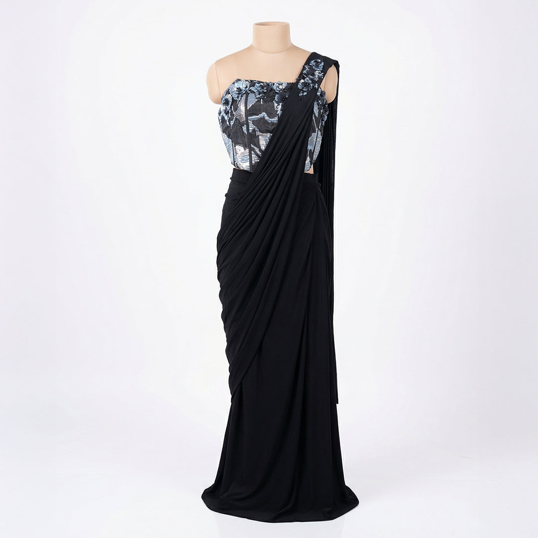 This is a stylish outfit is in a stunning black color. It features a trendy corset-style blouse with shiny silver patterns and beautiful flower designs on the shoulder.

It comes with a pre-draped saree that is very easy to wear and flows perfectly. This outfit is modern, fancy, and perfect for cocktail parties, receptions, and evening events.