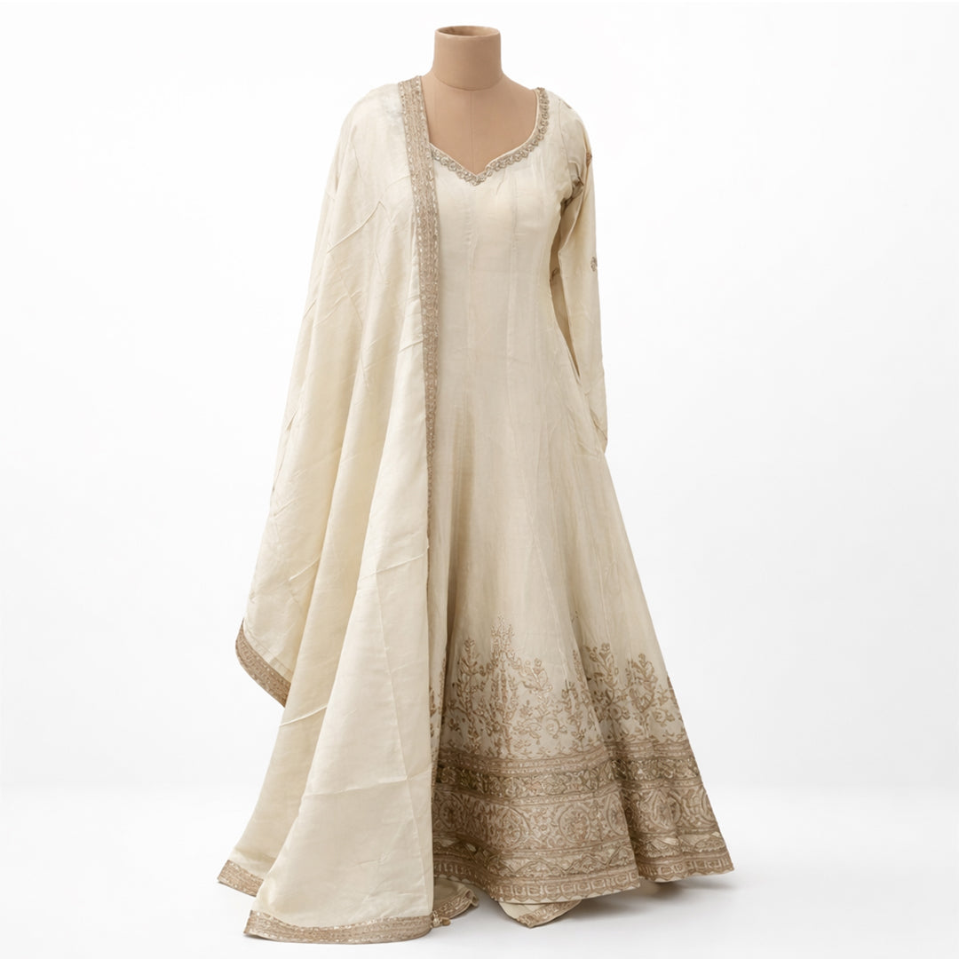 A timeless classic, this Off-White Silk Anarkali suit offers a graceful floor-length silhouette for the minimalist at heart. The suit is highlighted by a stunning antique gold Zardosi border and a traditional V-neckline, creating a look of understated luxury. Complete with a matching sheer dupatta and plazzo, it is the ultimate choice for day weddings, religious ceremonies, or intimate family gatherings.