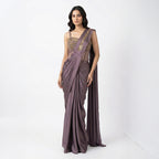 This stylish outfit is a pre-draped saree in a beautiful deep mauve color. It features a trendy corset-style blouse with thin straps and intricate gold embroidery on the upper part. The saree is draped perfectly with neat pleats in the front, and the fabric feels smooth and silky. The look is completed with an embroidered border on the shoulder drape, making it a modern and elegant choice for cocktail parties.