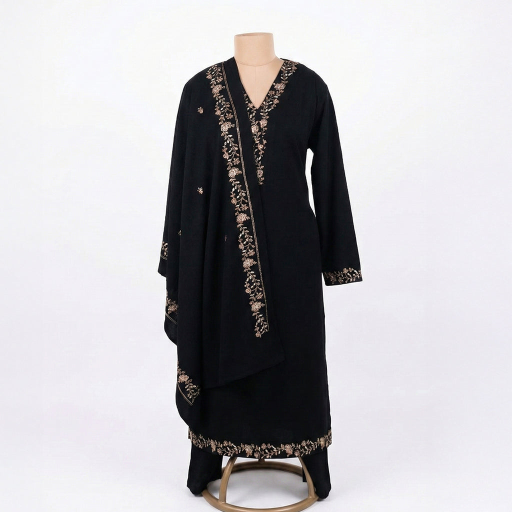 This classic outfit is in a deep black color. It is made from soft velvet fabric which is perfect for winter. The kurta has beautiful golden flower embroidery on the neckline, sleeves, and bottom hem. It comes with matching pants and a lovely shawl (dupatta) with a matching embroidered border. This outfit is simple, elegant, and great for evening parties and winter dinners.